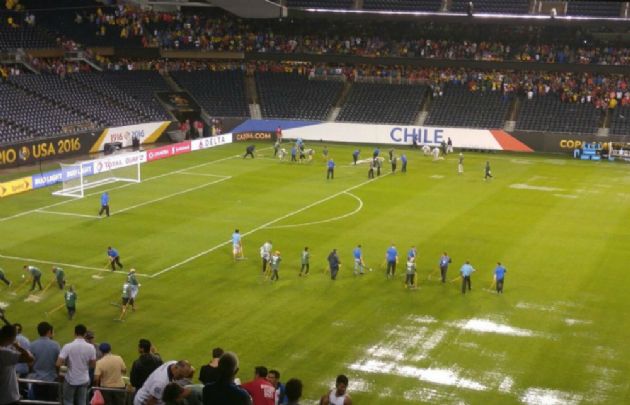 Operarios escurren la lluvia del campo de juego para la reanudación del partido. 