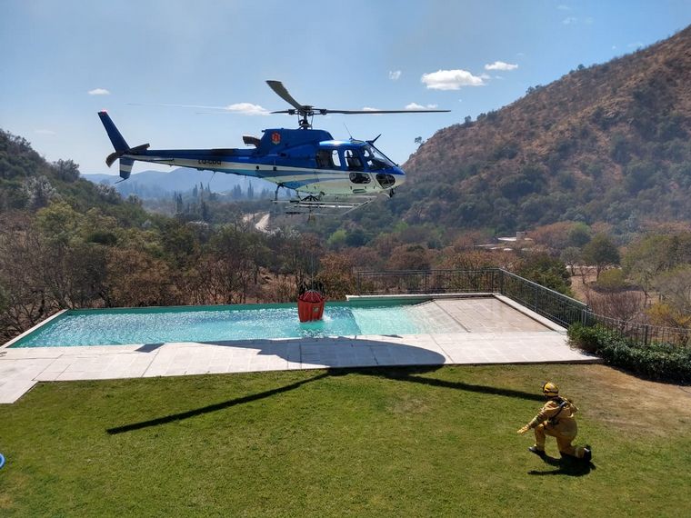 Un helicóptero, cargando agua en una pileta de una casa en La Paisanita.